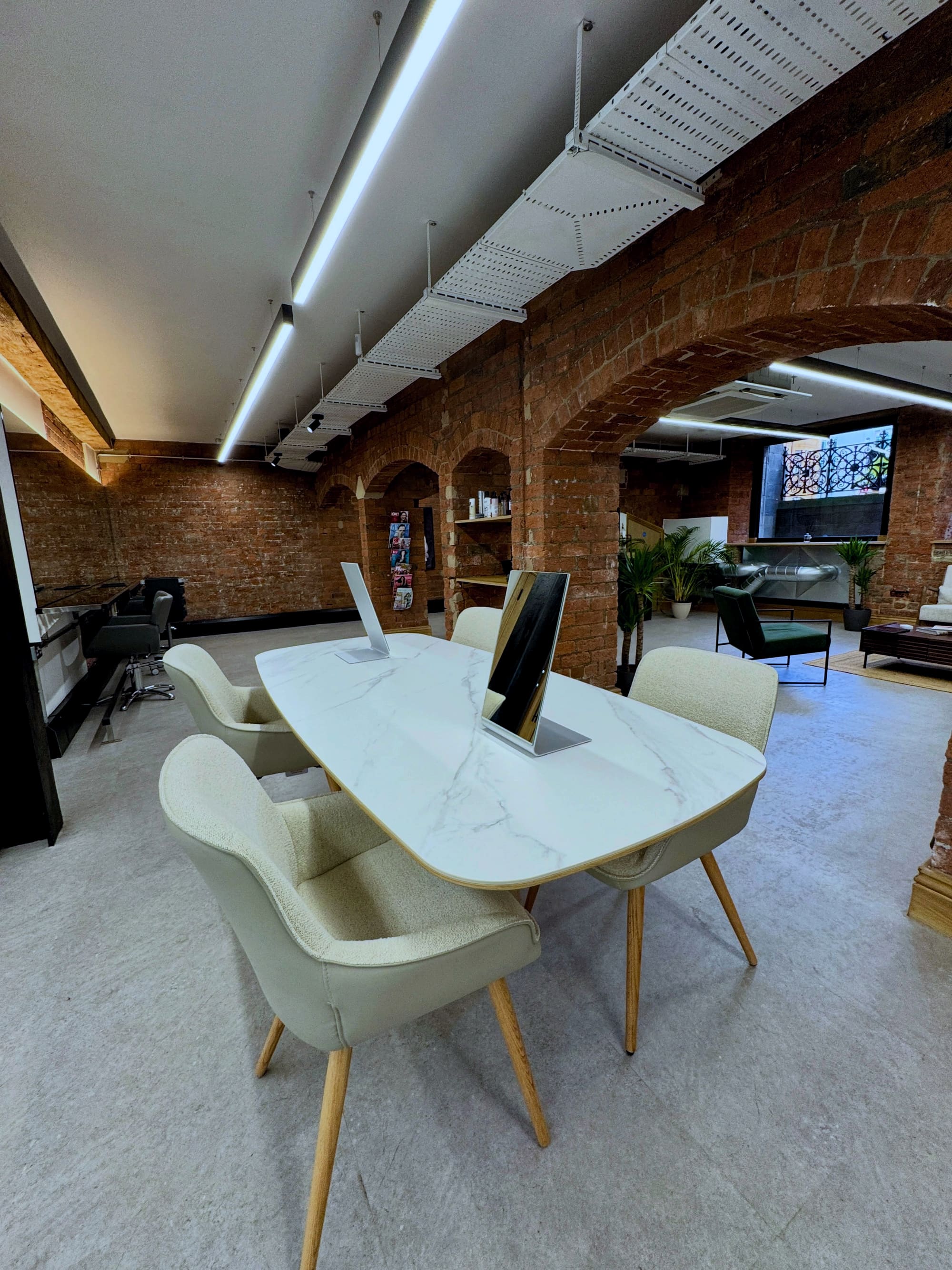 The salon floor: brick arches, a marble consultation table with mirrors, boucle chairs, and a green-velvet lounge beyond.