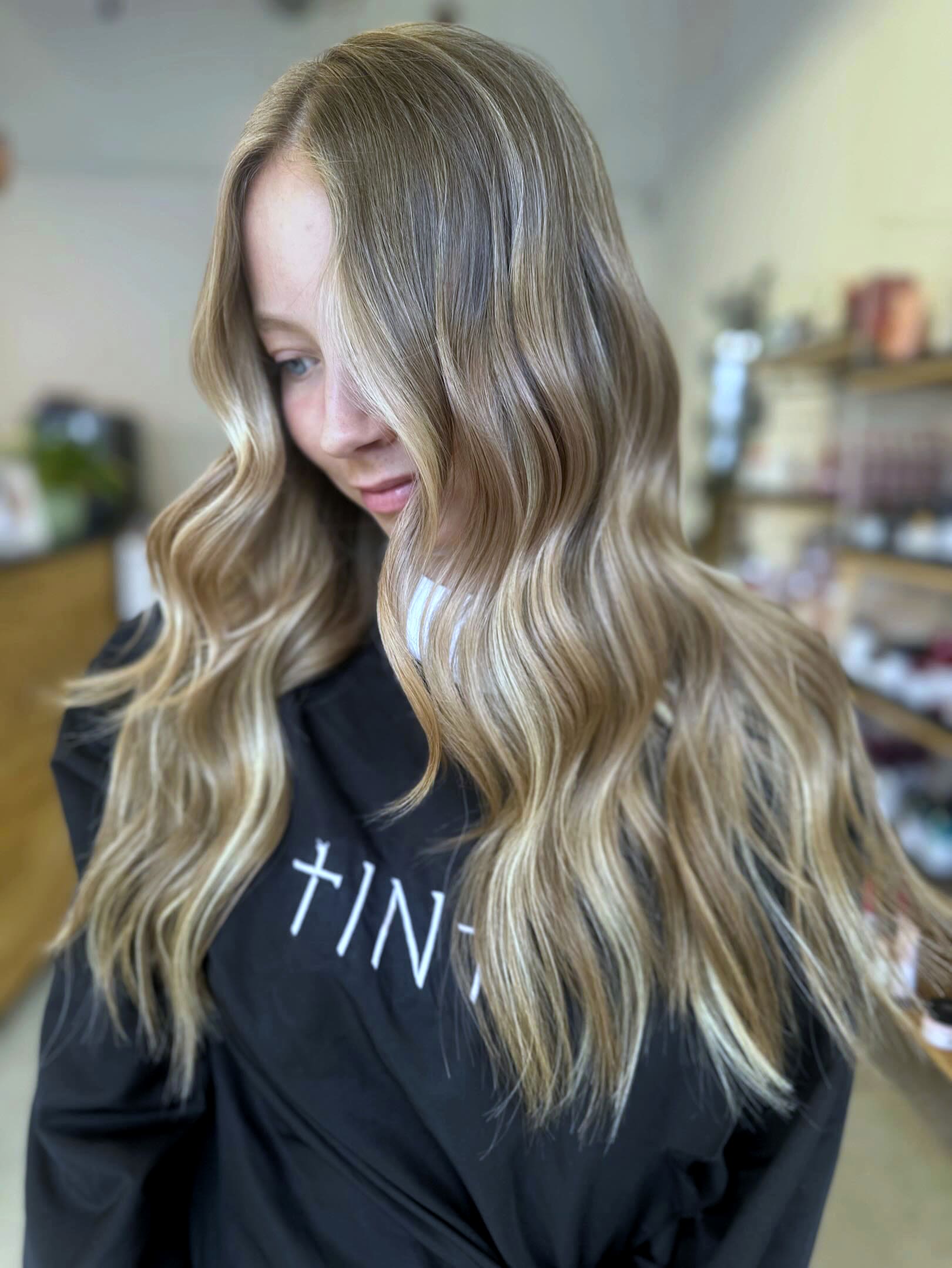 Soft blonde balayage waves over the black Tint cape.