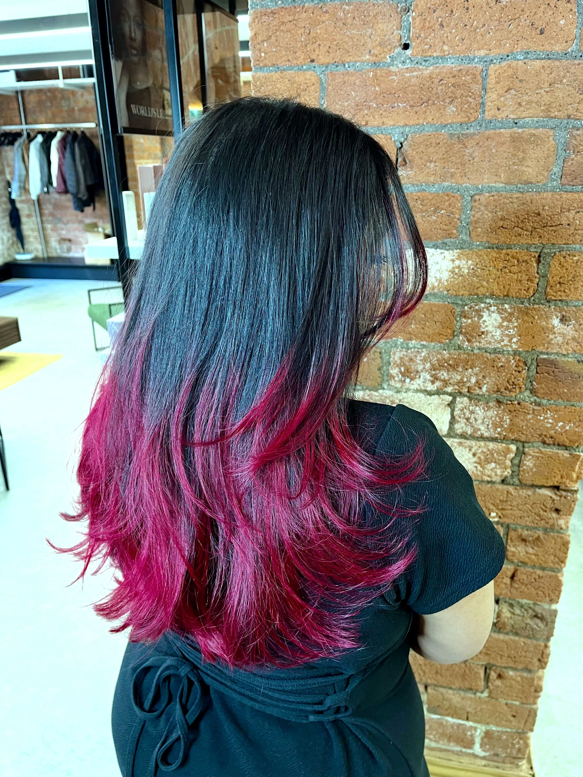 Black-to-raspberry dip-dye worn long, photographed from behind at the salon’s brick arch.
