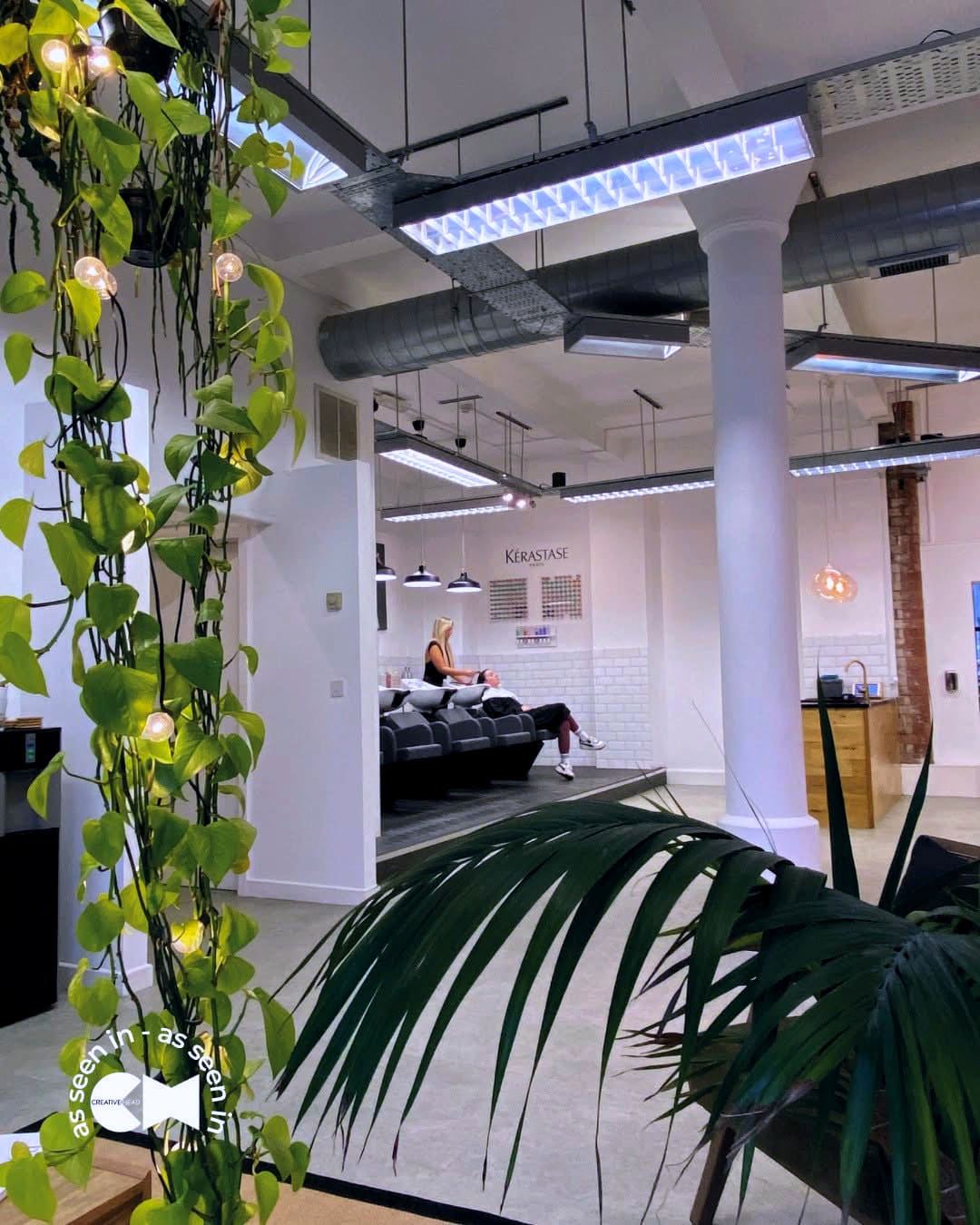 The backwash room — a white loft with vines over the basins and a client mid-wash; marked ‘as seen in Creative HEAD’.